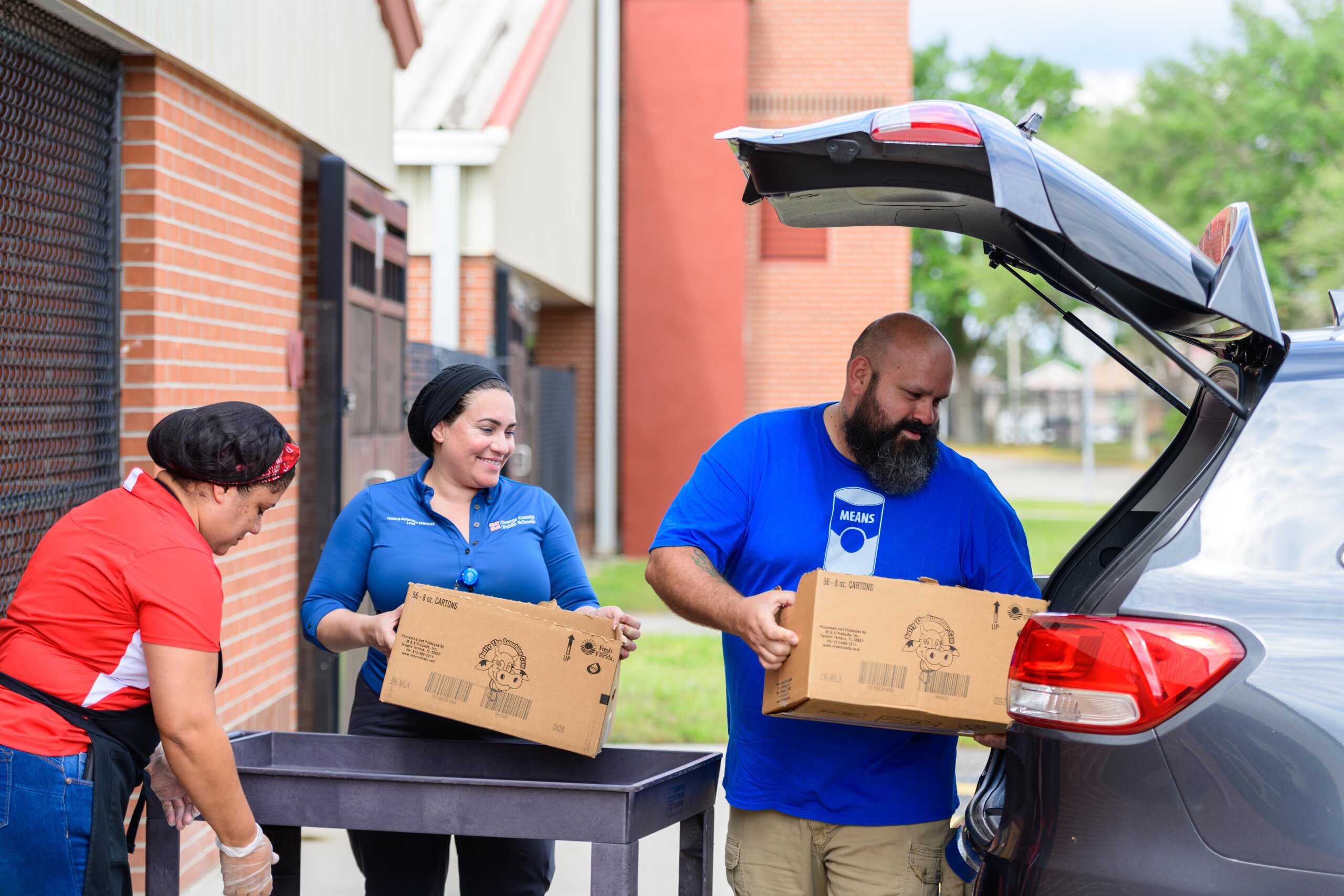 2023-04-14-MEANS-Database-Lake-Gem-Elementary-160-Edit Three people unloading a car with boxes of donated food.